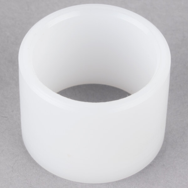 A white plastic bushing with a hole on a grey surface.
