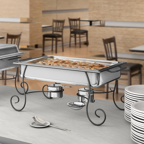 A buffet table with food and plates on a Choice chafing dish on a wrought iron stand.