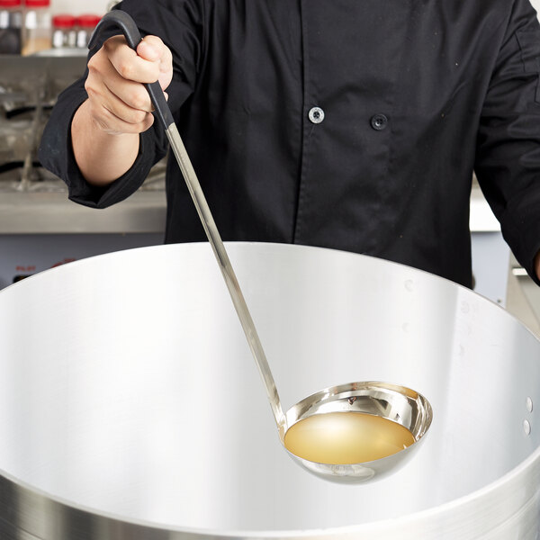 A person using a Vollrath Jacob's Pride ladle to pour liquid into a large pot.