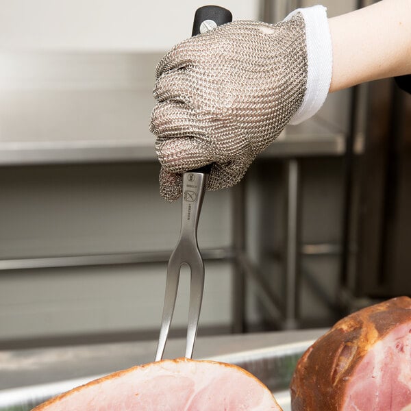 A hand holding a Mercer Culinary Genesis Forged Carving / Pot Fork over meat.