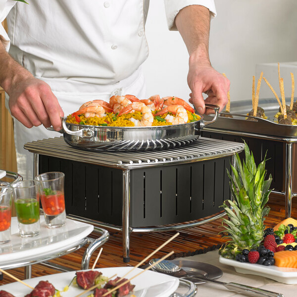 A chef using a Vollrath black buffet station to cook food on a grill.