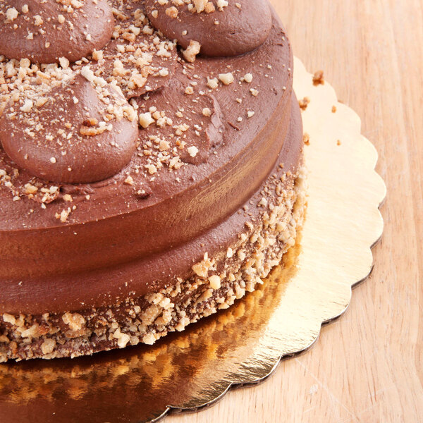 A 12" gold laminated corrugated cake circle with a chocolate cake with nuts on top.