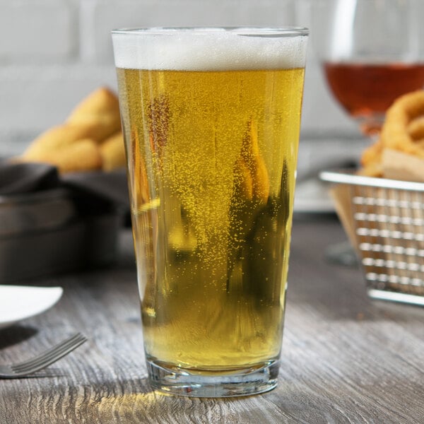 An Anchor Hocking rim tempered mixing glass full of beer sits on a table in a bar.