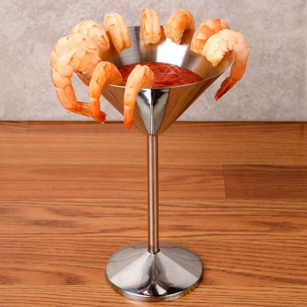 A martini glass with shrimp and sauce served in a metal cup with a metal base.