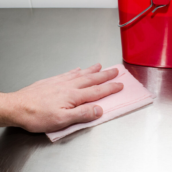A hand using a Chicopee pink medium-duty towel to wipe a metal surface.
