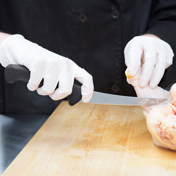A person in white gloves using a Mercer Culinary Millennia Curved Stiff Boning Knife to cut chicken.