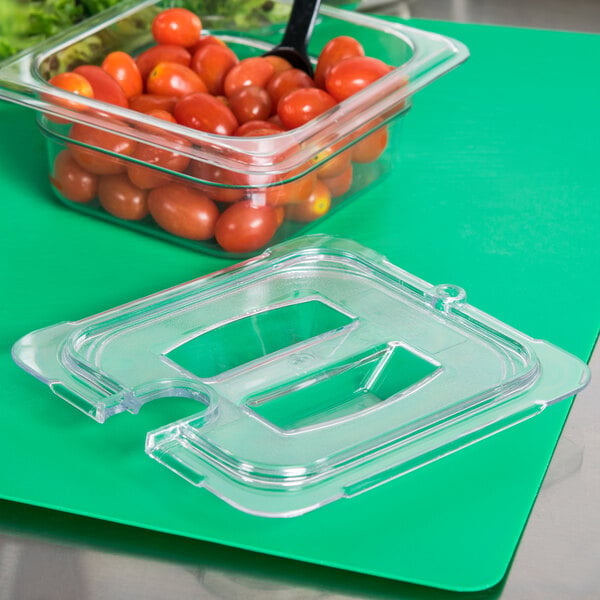 A Carlisle clear plastic food pan lid with a spoon notch on a container of cherry tomatoes.