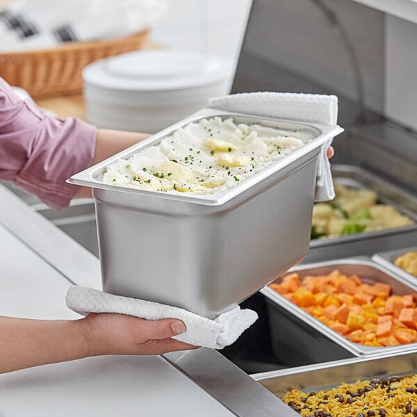 A person holding a container of food in a stainless steel steam table pan.