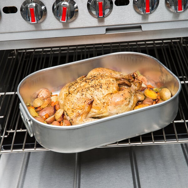 A Vollrath Wear-Ever aluminum roasting pan with a roast chicken and potatoes in it on an oven.