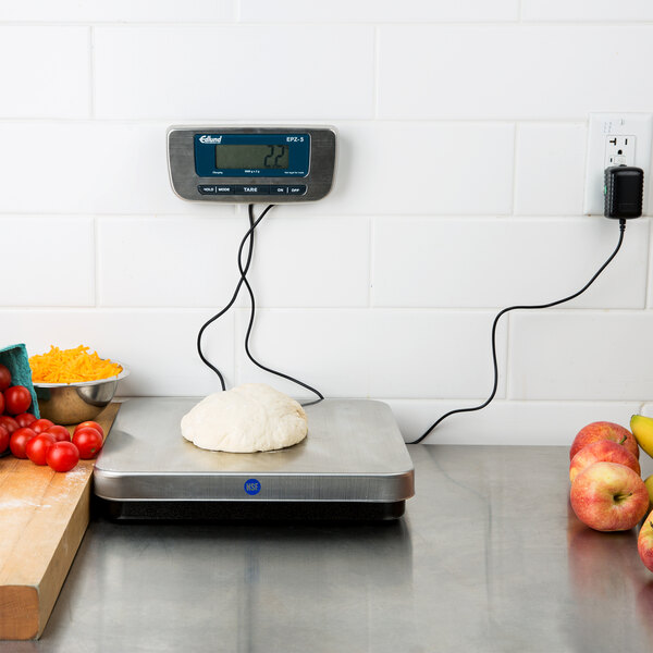 A stainless steel Edlund digital pizza scale on a kitchen counter with dough on it.
