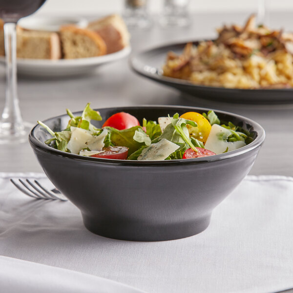 A Tuxton black china bowl filled with salad, tomatoes, and cheese on a table.