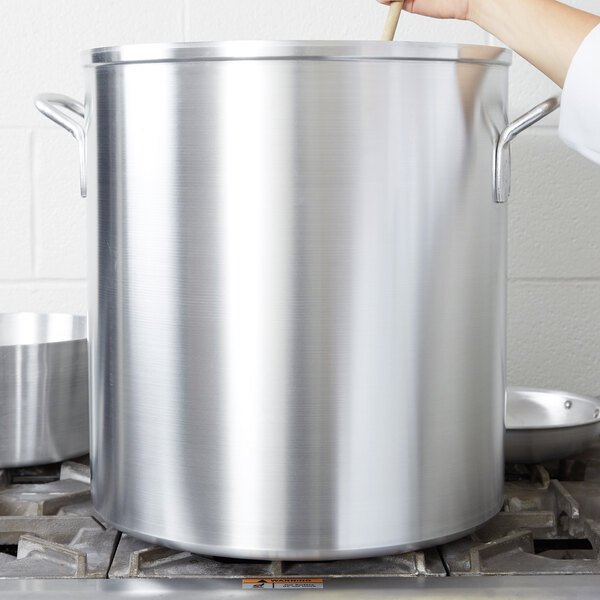 A woman stirring a large Vollrath Wear-Ever aluminum stock pot with a wooden spoon.