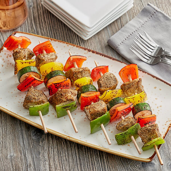 A plate with Royal Paper Eco-Friendly Wood Skewers of meat and vegetables on a table.