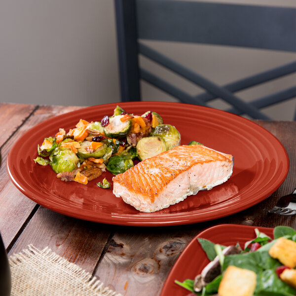 A close-up of Fiesta® Scarlet China Round Chop Plate with salmon and vegetables on a table.