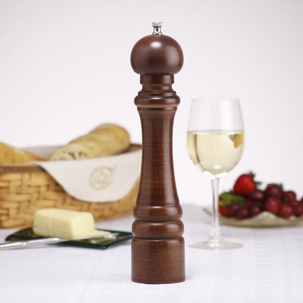 A Chef Specialties walnut pepper mill next to a glass of wine.