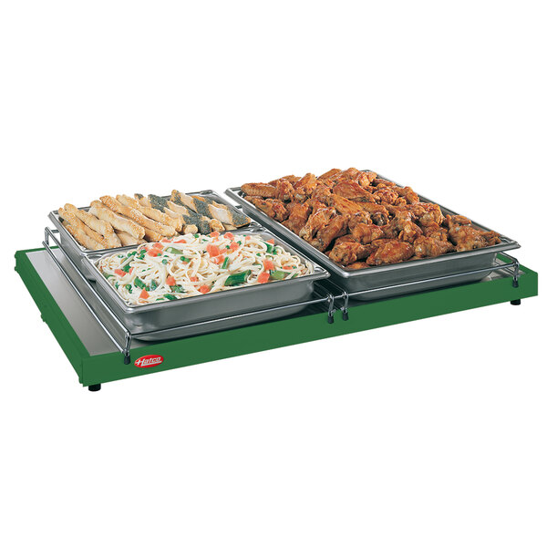 A Hatco heated shelf with trays of chicken wings, pasta, and bread sticks on a table.