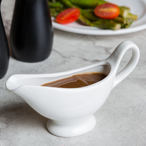 An American Metalcraft white porcelain gravy boat with brown sauce in it.