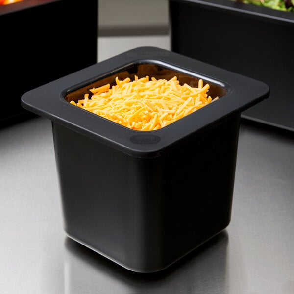 A black Cambro food pan containing yellow cheese on a counter in a salad bar.