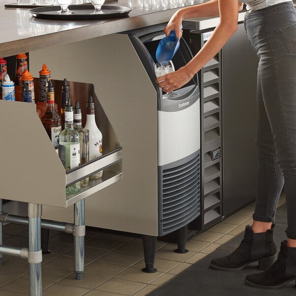 A woman standing next to a Scotsman undercounter ice machine on a counter.