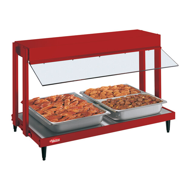 A red Hatco countertop food warmer with two trays of food on a buffet.