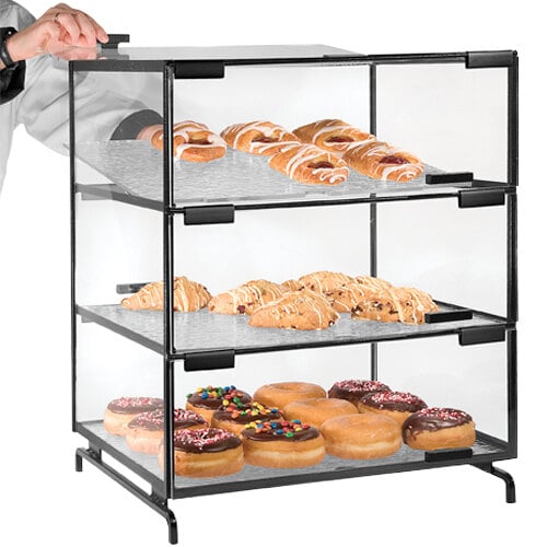 A person holding a Cal-Mil black pastry display case with doughnuts.
