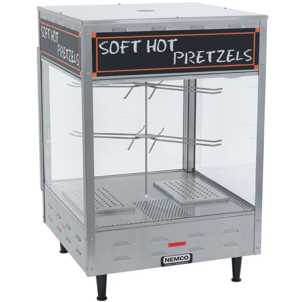A Nemco revolving pretzel merchandiser with a sign on it displaying soft hot pretzels.
