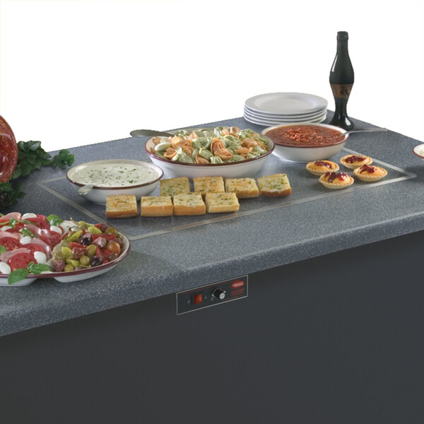 A table with a Hatco heated stone shelf holding plates of food and a bottle of soda.
