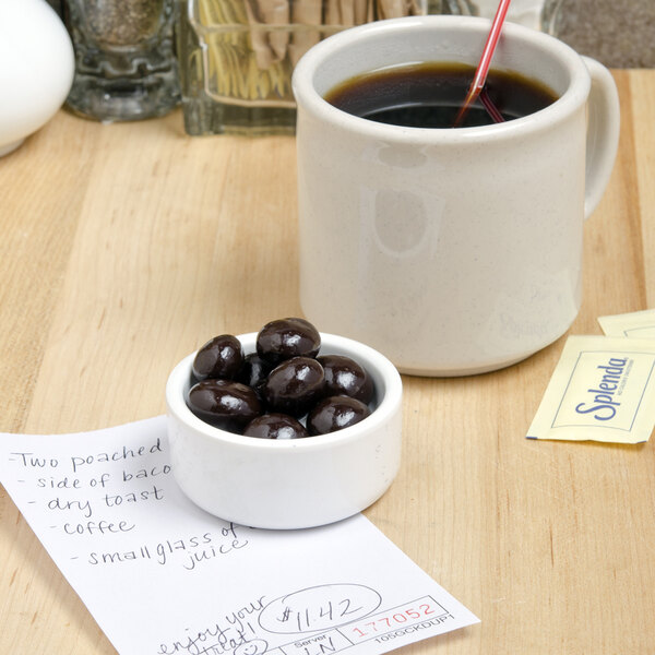 A bowl of DaVinci Gourmet dark chocolate covered espresso beans on a table with a cup of coffee.