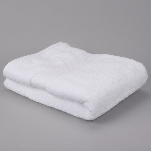 A folded white Oxford Miasma bath towel on a gray surface.