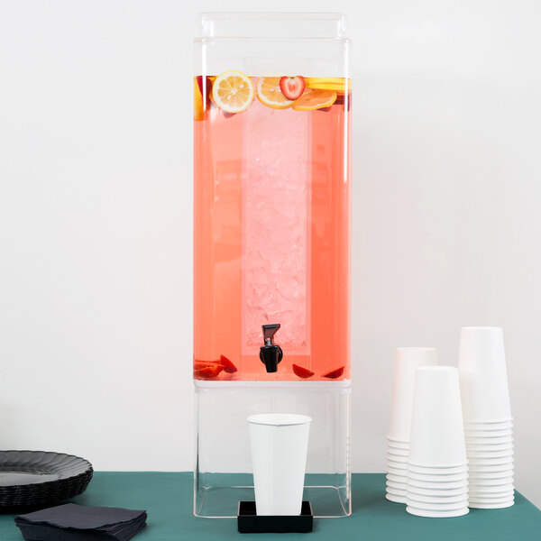 A clear Cal-Mil beverage dispenser with a drink and cups underneath.