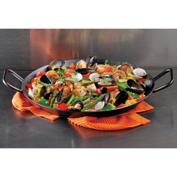 A Lodge carbon steel paella pan full of seafood and vegetables on a table.