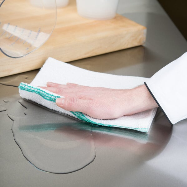 A hand with a green and white striped Chef Revival bar towel cleaning a counter.