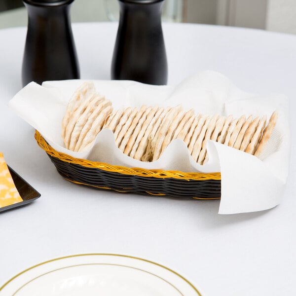 A black and gold rattan cracker basket on a table full of crackers.