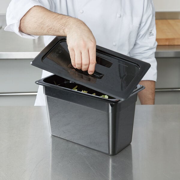 A chef putting food into a black container with a Cambro black polycarbonate lid.