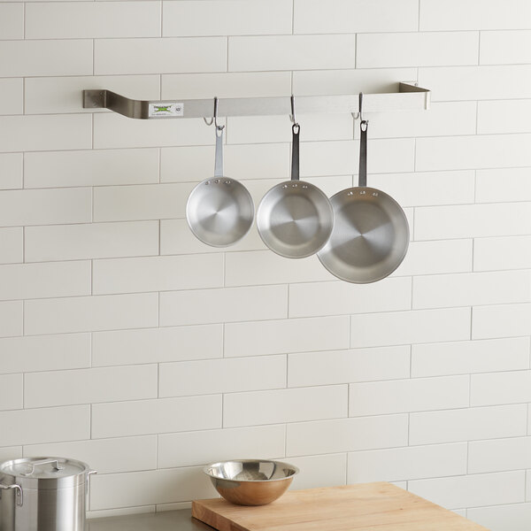 A Regency stainless steel wall mounted pot rack with pans hanging.
