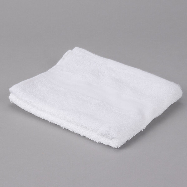 An Oxford Gold white hand towel with a cam border folded on a gray surface.