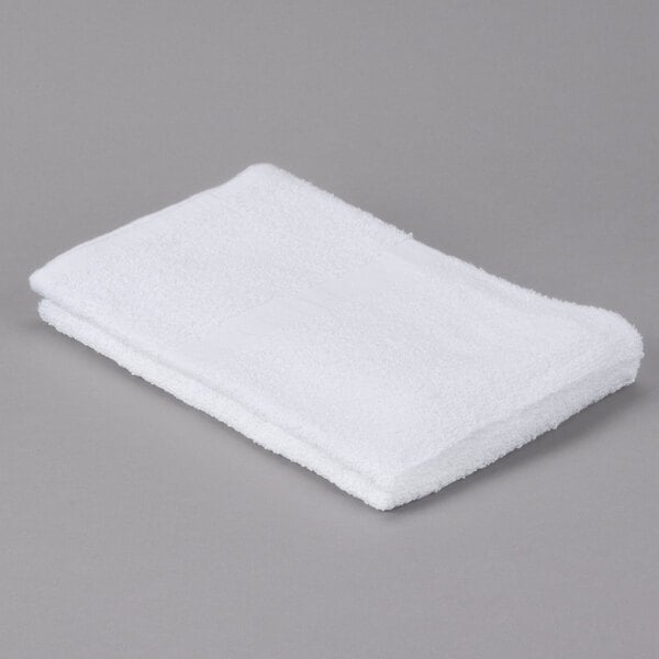 An Oxford Gold white bath towel with a cam border on a gray surface.