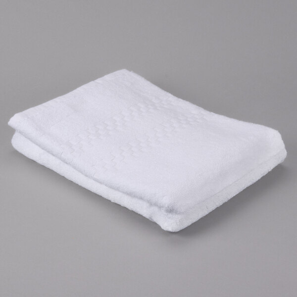 A folded white Oxford Viceroy terry bath towel with a dobby checkered border and dobby twill hem on a gray surface.