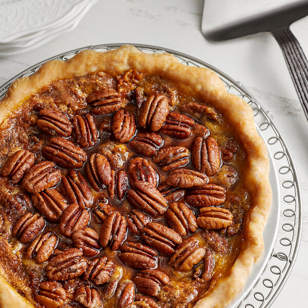 A pecan pie with Jr. Mammoth Raw Pecan Halves on top on a plate.