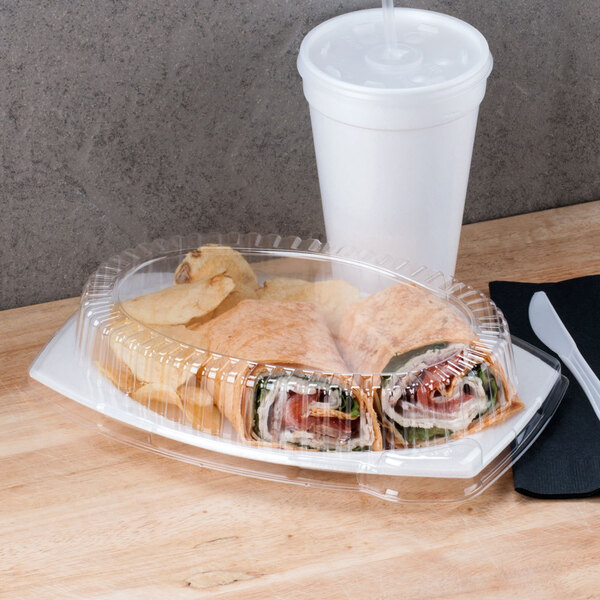 A wrap sandwich in a Dart clear plastic container next to a white cup of chips.