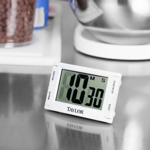 A Taylor digital kitchen timer with a white clock face and black numbers on a counter.