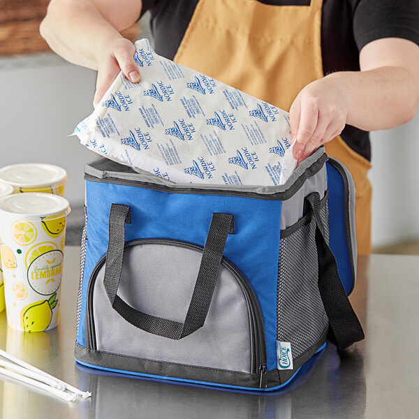 A woman opening a blue and grey Choice insulated cooler bag with a brick cold pack inside.