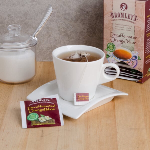 A cup of Bromley decaffeinated tea with a tea bag on a saucer next to a box of Bromley Exotic Orange Pekoe Decaffeinated Tea.