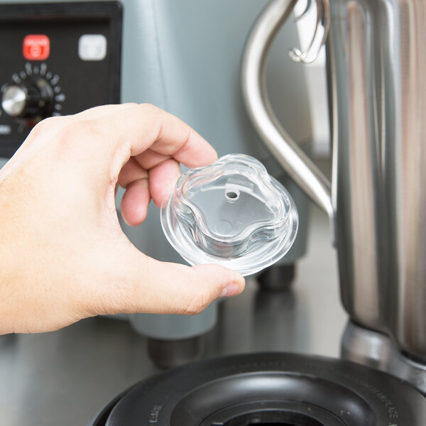 A hand holding a clear plastic cover over a blender.