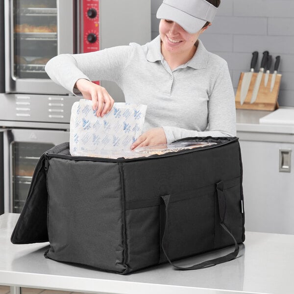 A woman using a Choice insulated food delivery bag to put food in a plastic container.