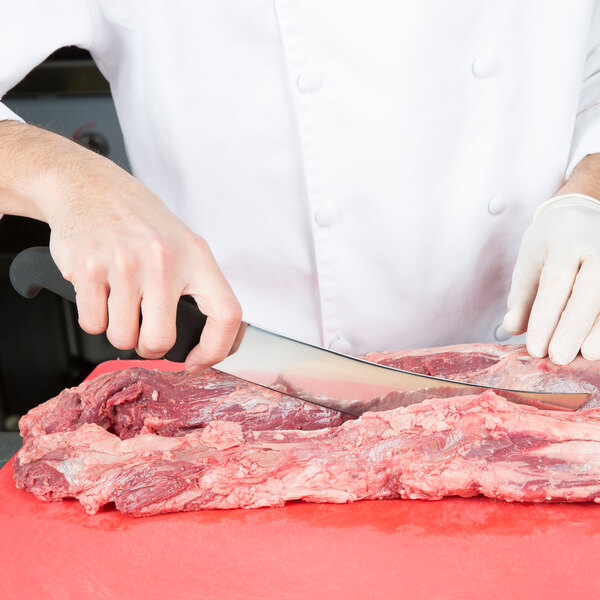 A person using a Victorinox Cimeter Knife to cut meat on a table.