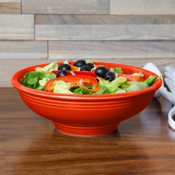 A Fiesta china pedestal serving bowl filled with salad and vegetables on a table.