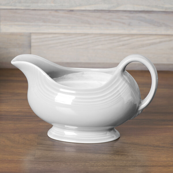 A Fiesta white China gravy boat on a wood surface.
