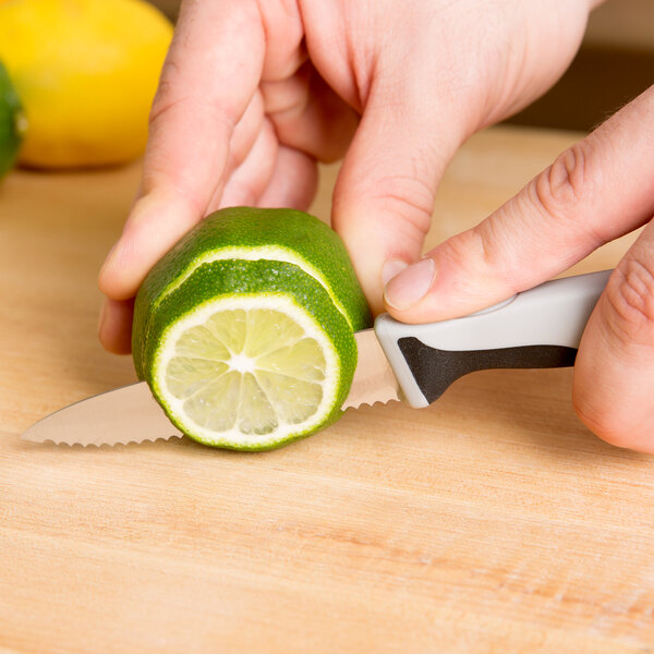 A hand holding a Mercer Culinary Millennia Serrated Edge Paring Knife cutting a lime on a counter.