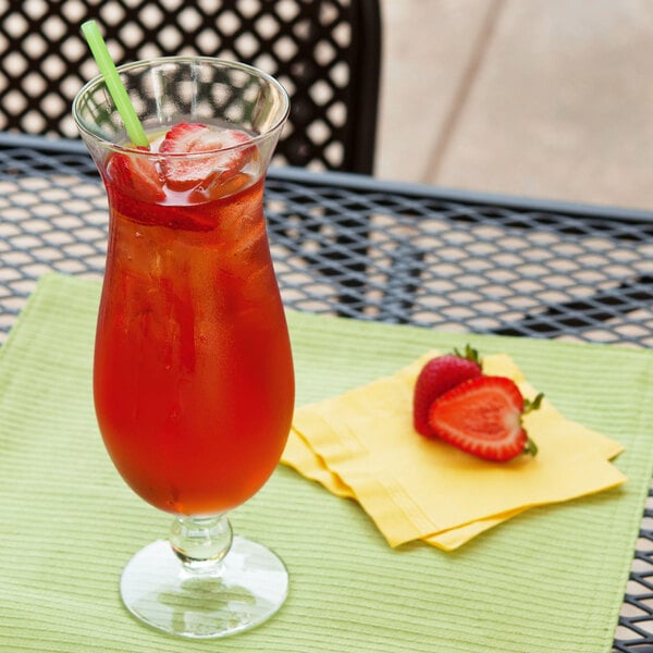 A GET plastic hurricane glass filled with red liquid and strawberries with a straw on a napkin.